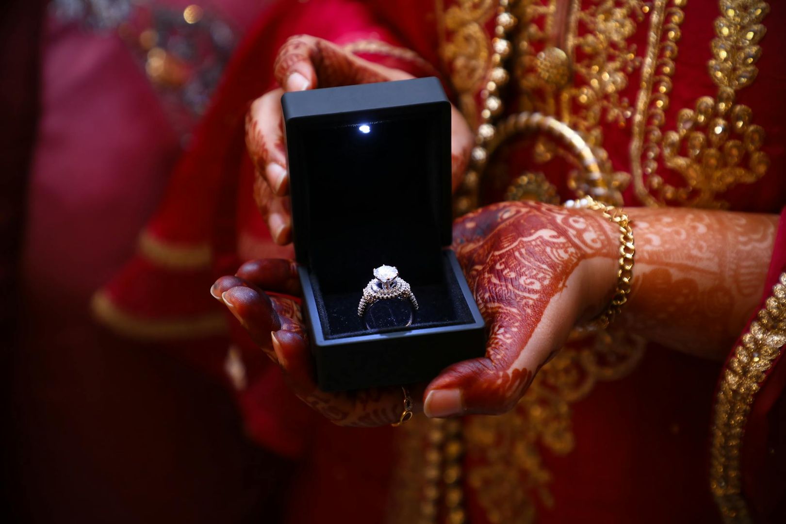 Händer med hennatatueringar håller en öppen svart låda med en glittrande diamantring.