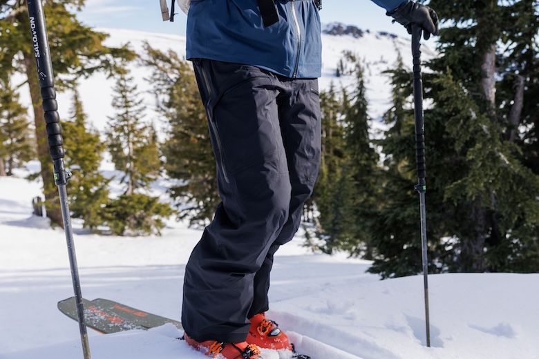 Person i skidkläder och pjäxor står med stavar i snöiga fjäll.